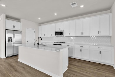 Kitchen featuring appliances with stainless steel finishes, white cabinetry, light wood finished floors, decorative backsplash, and recessed lighting