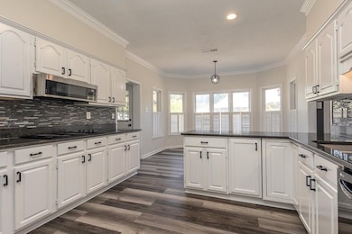 Kitchen with backsplash, dark stone counters, white cabinets, ornamental molding, and stainless steel microwave