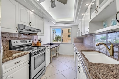Kitchen with electric range, under cabinet range hood, a tray ceiling, backsplash, and ceiling fan