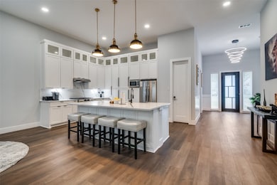 Kitchen with pendant lighting, a breakfast bar, white cabinets, an island with sink, and recessed lighting