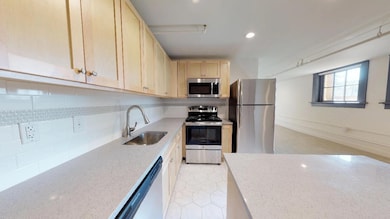 Kitchen featuring light brown cabinets, tasteful backsplash, light stone countertops, appliances with stainless steel finishes, and sink