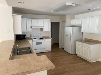 Kitchen with white appliances, dark wood-style floors, white cabinets, light countertops, and under cabinet range hood