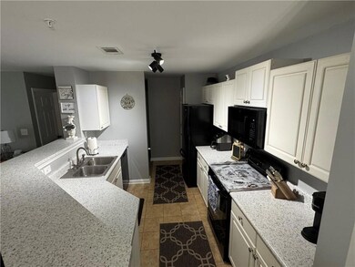 Kitchen with black appliances, a sink, a peninsula, white cabinetry, and light tile patterned floors