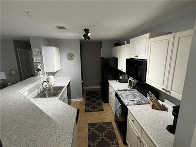 Kitchen with black appliances, a sink, a peninsula, white cabinetry, and light tile patterned floors
