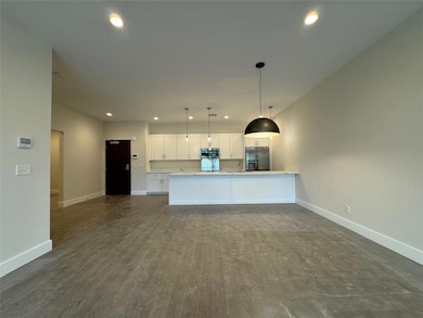 Kitchen with stainless steel appliances, white cabinetry, open floor plan, recessed lighting, and decorative light fixtures