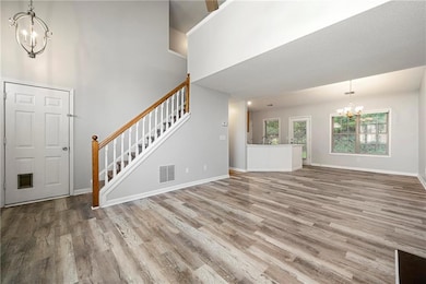 Unfurnished living room with a chandelier, wood finished floors, a towering ceiling, and stairs