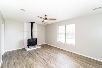 Unfurnished living room featuring a wood stove, wood finished floors, and baseboards