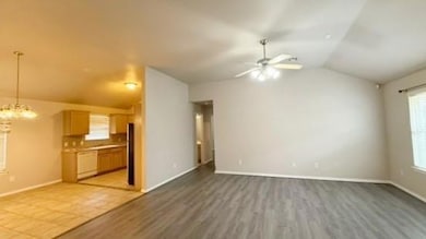 Unfurnished living room featuring vaulted ceiling, a ceiling fan, light wood finished floors, and a chandelier