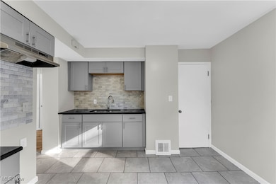 Kitchen featuring gray cabinetry, backsplash, under cabinet range hood, and light tile patterned floors