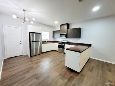 Kitchen featuring an inviting chandelier, a peninsula, dark wood-style floors, dark countertops, and appliances with stainless steel finishes