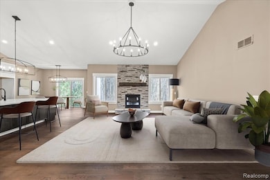 Living room featuring a stone fireplace, dark wood finished floors, a chandelier, recessed lighting, and high vaulted ceiling