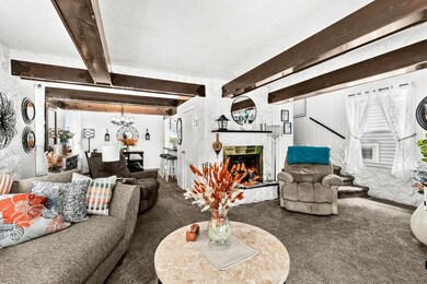 Carpeted living area featuring beam ceiling, a fireplace, a chandelier, and a textured ceiling