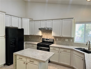 Kitchen with black fridge, light tile patterned flooring, decorative backsplash, a center island, and white cabinetry