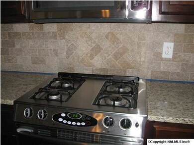 Kitchen with stainless steel appliances, tumbled travertine backsplash, Granite counter tops, and hardwood flooring.