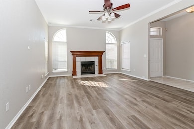 Unfurnished living room featuring a fireplace, ceiling fan, light wood-type flooring, and crown molding