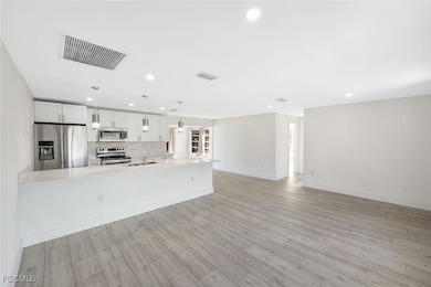 Kitchen featuring appliances with stainless steel finishes, white cabinetry, backsplash, open floor plan, and recessed lighting