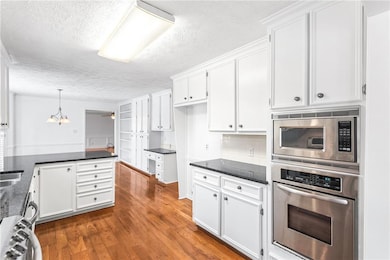 Kitchen with stainless steel appliances, a peninsula, white cabinetry, a textured ceiling, and dark wood-style flooring