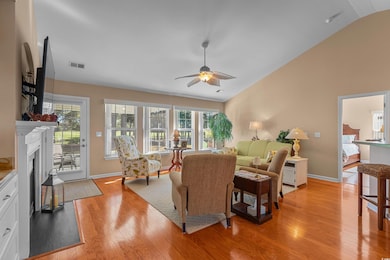 Living room featuring light wood-style flooring, a fireplace with flush hearth, a ceiling fan, and high vaulted ceiling