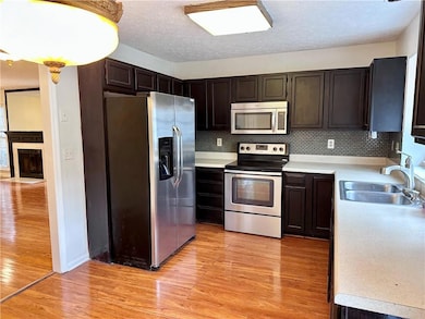 Kitchen with stainless steel appliances, light countertops, light wood-style flooring, decorative backsplash, and a sink