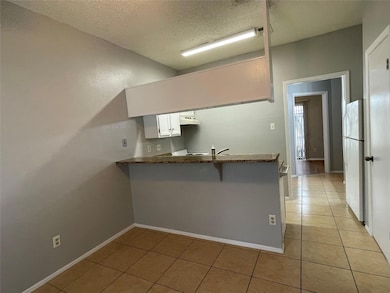 Kitchen featuring a textured ceiling, light tile patterned floors, freestanding refrigerator, a peninsula, and a breakfast bar