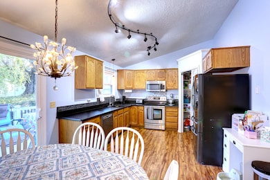 Kitchen with dark countertops, appliances with stainless steel finishes, a textured ceiling, vaulted ceiling, and brown cabinetry