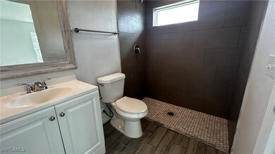 Bathroom with vanity, tiled shower, wood-type flooring, and toilet