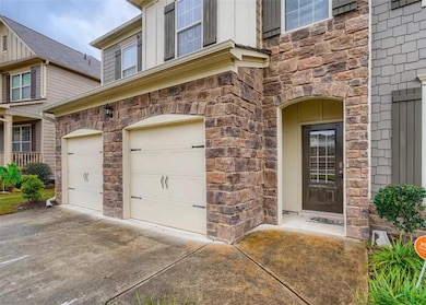 Property entrance with an attached garage, stone siding, and driveway