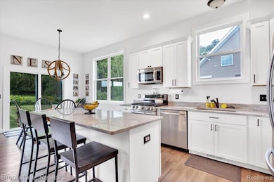 Kitchen with neutral white cabinetry, light wood-flooring, a breakfast bar, stone counters, and recessed lighting