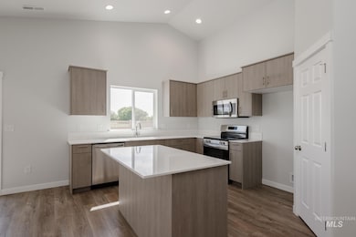 Kitchen featuring modern cabinets, appliances with stainless steel finishes, dark wood-style floors, high vaulted ceiling, and a kitchen island
