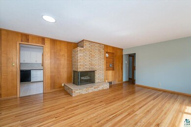 Unfurnished living room with a brick fireplace, wood finished floors, visible vents, and baseboards