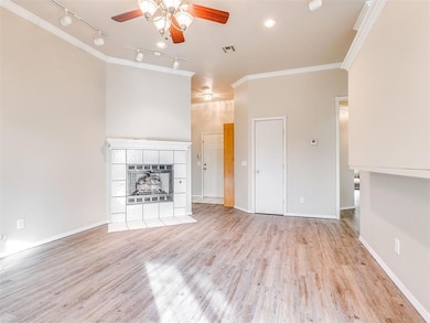Unfurnished living room with a ceiling fan, rail lighting, ornamental molding, light wood-style flooring, and a tile fireplace