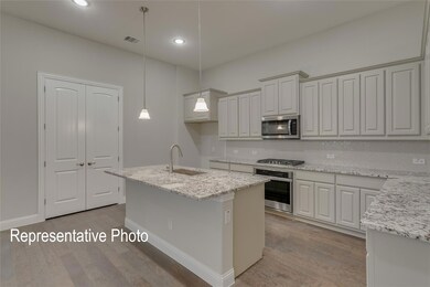 Kitchen with a kitchen island with sink, sink, light wood-type flooring, decorative light fixtures, and stainless steel appliances