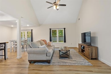 Living room with high vaulted ceiling, light wood finished floors, a ceiling fan, and french doors
