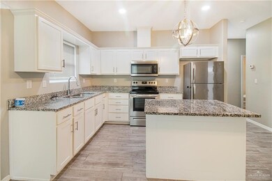 Kitchen featuring light wood-type flooring, light stone counters, stainless steel appliances, sink, and hanging light fixtures