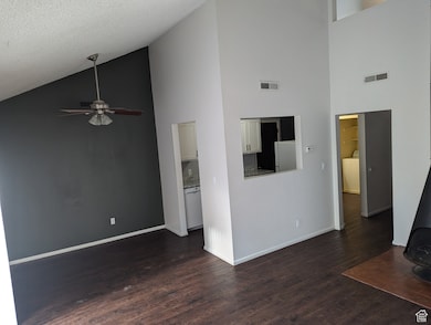 Unfurnished living room featuring high vaulted ceiling, dark wood finished floors, a ceiling fan, and a textured ceiling
