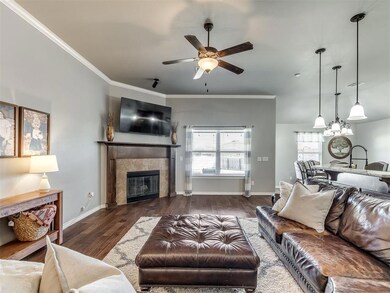 Living room with dark hardwood / wood-style flooring, ceiling fan with notable chandelier, a fireplace, and crown molding
