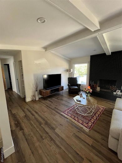 Living room with beamed ceiling, a fireplace, and dark wood-style floors