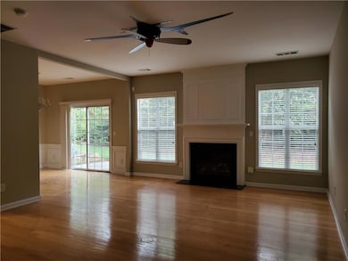 Unfurnished living room featuring ceiling fan, wood finished floors, a large fireplace, wainscoting, and a decorative wall