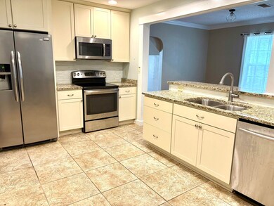 Kitchen with appliances with stainless steel finishes, crown molding, tasteful backsplash, light tile patterned floors, and light stone counters