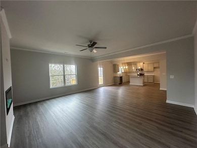 Unfurnished living room featuring dark wood-style floors, ornamental molding, and baseboards