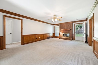 Unfurnished living room featuring crown molding, light carpet, a ceiling fan, a wainscoted wall, and a fireplace