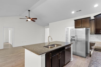 Kitchen featuring appliances with stainless steel finishes, a ceiling fan, light wood-style flooring, dark stone countertops, and vaulted ceiling