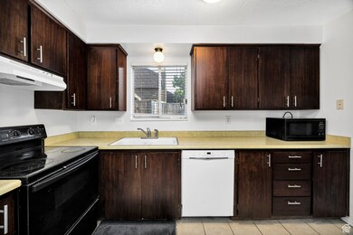 Kitchen featuring black appliances, light countertops, under cabinet range hood, and dark brown cabinets