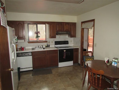 Kitchen featuring white appliances, light countertops, backsplash, and under cabinet range hood