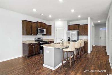 Kitchen featuring appliances with stainless steel finishes, light stone countertops, a breakfast bar, dark wood finished floors, and dark brown cabinets