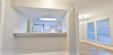 Kitchen featuring white appliances, a skylight, white cabinets, light wood-type flooring, and a chandelier