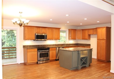 Kitchen with appliances with stainless steel finishes, dark countertops, brown cabinets, and light hardwood floors