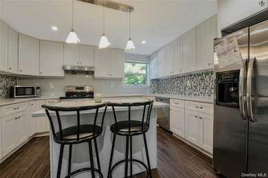 Kitchen with stainless steel appliances, a breakfast bar, decorative backsplash, decorative light fixtures, and white cabinets