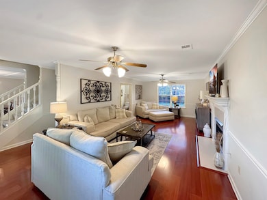 Living area featuring stairway, dark wood-style flooring, a fireplace, ornamental molding, and a ceiling fan