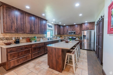 Kitchen featuring stainless steel appliances, a kitchen bar, dark brown cabinetry, decorative backsplash, and recessed lighting